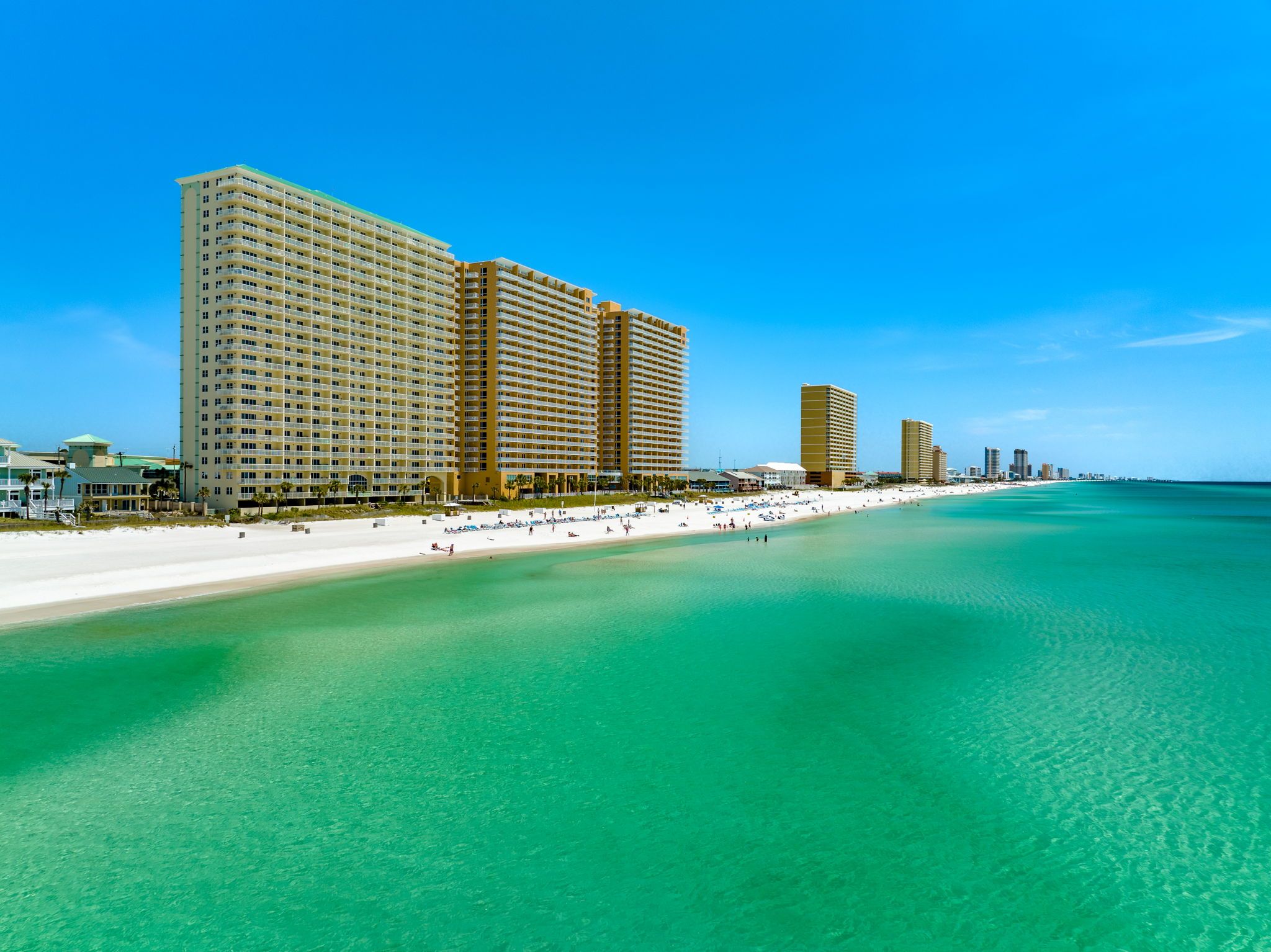 Een hotel aan het strand met meerdere hoge gebouwen, een zandstrand en helder turquoise water.