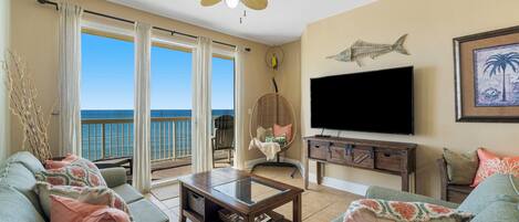 A living room with a large window, a ceiling fan, a flat-screen TV, and a wooden cabinet.