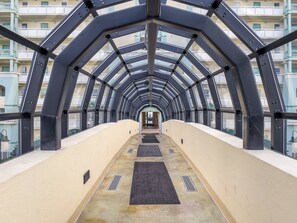 A covered walkway with a metal framework and glass panels, leading to a building entrance.