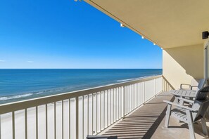 Un balcon avec vue sur l’océan, une balustrade blanche et deux chaises.