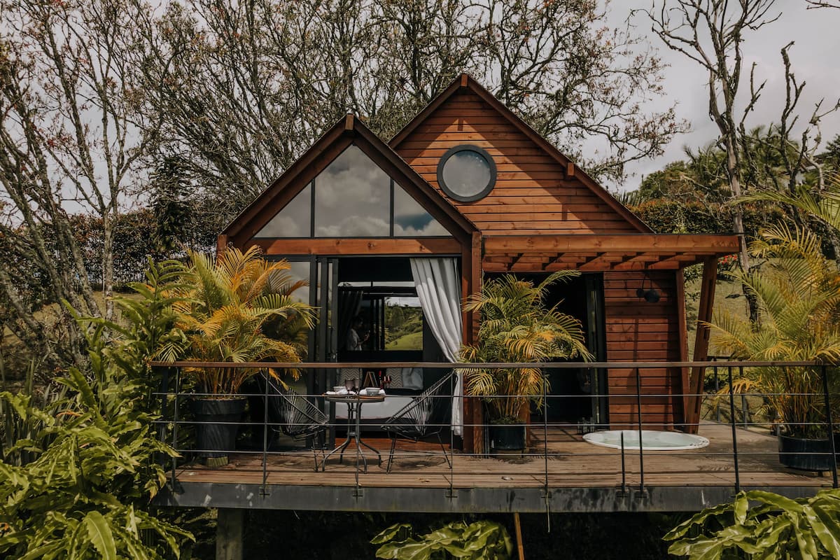A wooden cabin with a large window, a circular skylight, and a deck with chairs and a table.