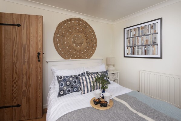 A neatly arranged bedroom with a bed, a round woven wall hanging, a framed bookshelf, and a wooden wardrobe. - Tathra Beach Cottage - a cottage that sleeps 5 guests in 3 bedrooms (St Ives)