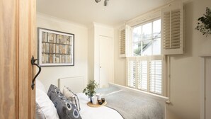 Une chambre à coucher comprenant un lit, une table de chevet, un radiateur, une fenêtre avec des volets et un tableau encadré accroché au mur.