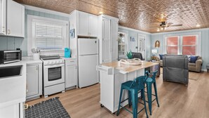 A compact kitchen with white cabinets, a microwave, stove, and a refrigerator. There's a small dining area with a wooden table and teal chairs. - Rocks On The Side: Private Pool, Steps to the Beach, Murrells Inlet (Murrells Inlet)