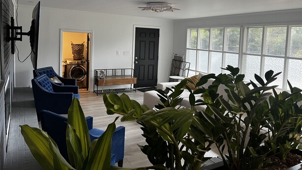 Ein geräumiges Wohnzimmer mit großem Fenster, einer schwarzen Tür und einem Deckenventilator.