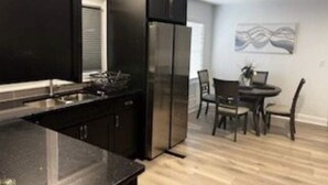 Eine moderne Küche mit schwarzen Schränken, einem Edelstahl-Kühlschrank und einem Essbereich mit Tisch und Stühlen.