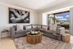 A modern living room with a grey sectional sofa, a round wooden coffee table, and a large abstract painting.