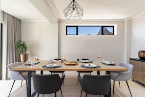 A dining area with a wooden table, grey chairs, a potted plant, and a view of the mountains through a window.