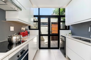 A modern kitchen with a stove, oven, and sink, and a glass door leading to an outdoor area.