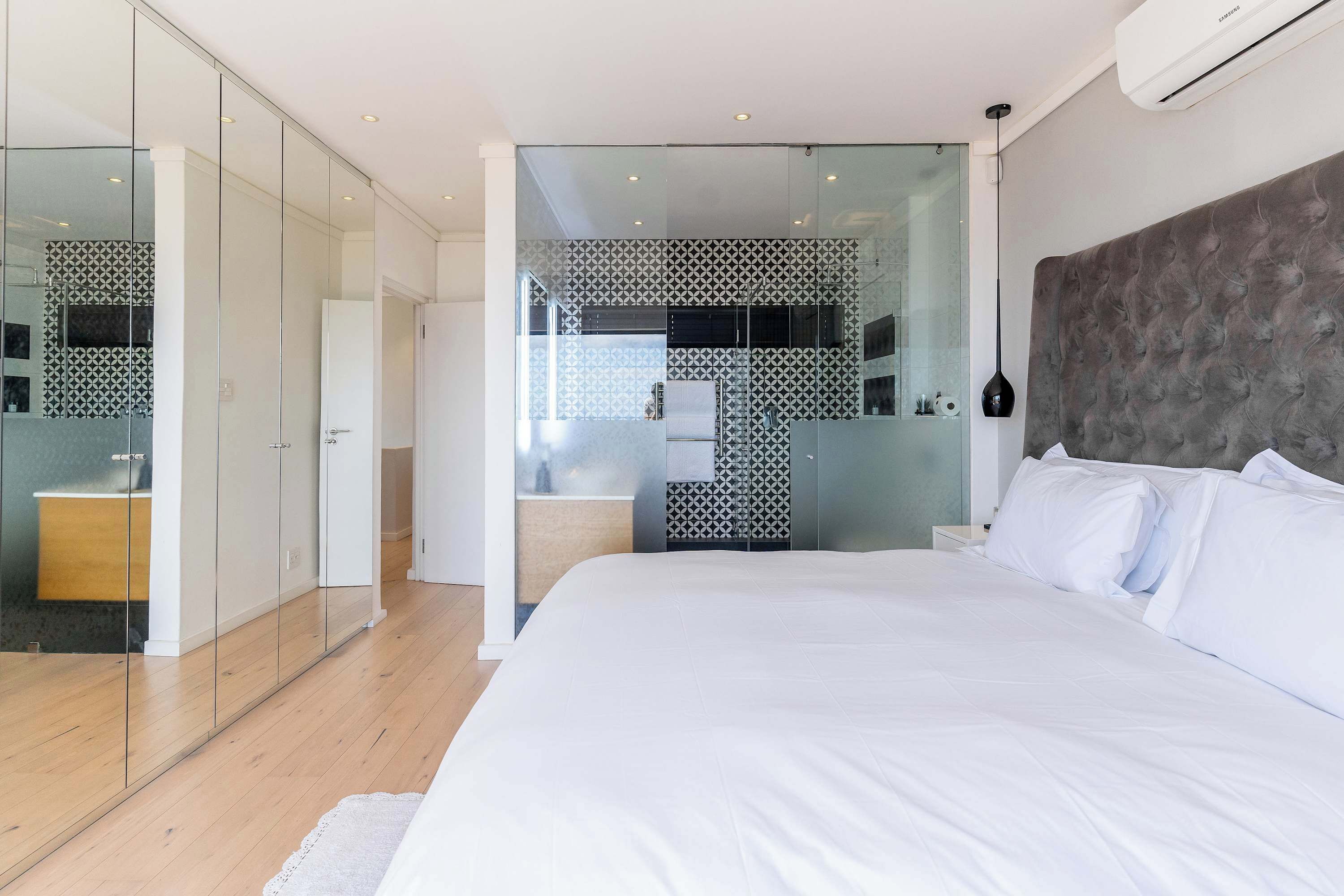 A modern bedroom with a large bed, a glass partition wall, and a built-in wardrobe.