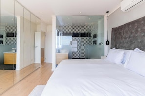 A modern bedroom with a large bed, a glass partition wall, and a built-in wardrobe.