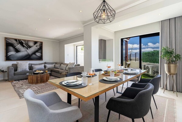 A modern living room with a dining area, a large abstract painting, and a view of the outdoors.