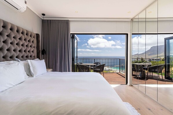 A bedroom with a large bed, a view of the ocean, and a balcony with outdoor seating.