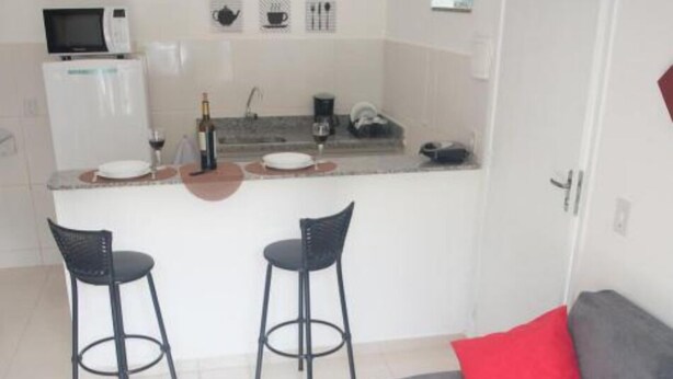 A compact kitchen with a microwave, wine bottle, and bar stools. - Apart Sol Nascente (Itatiaia)