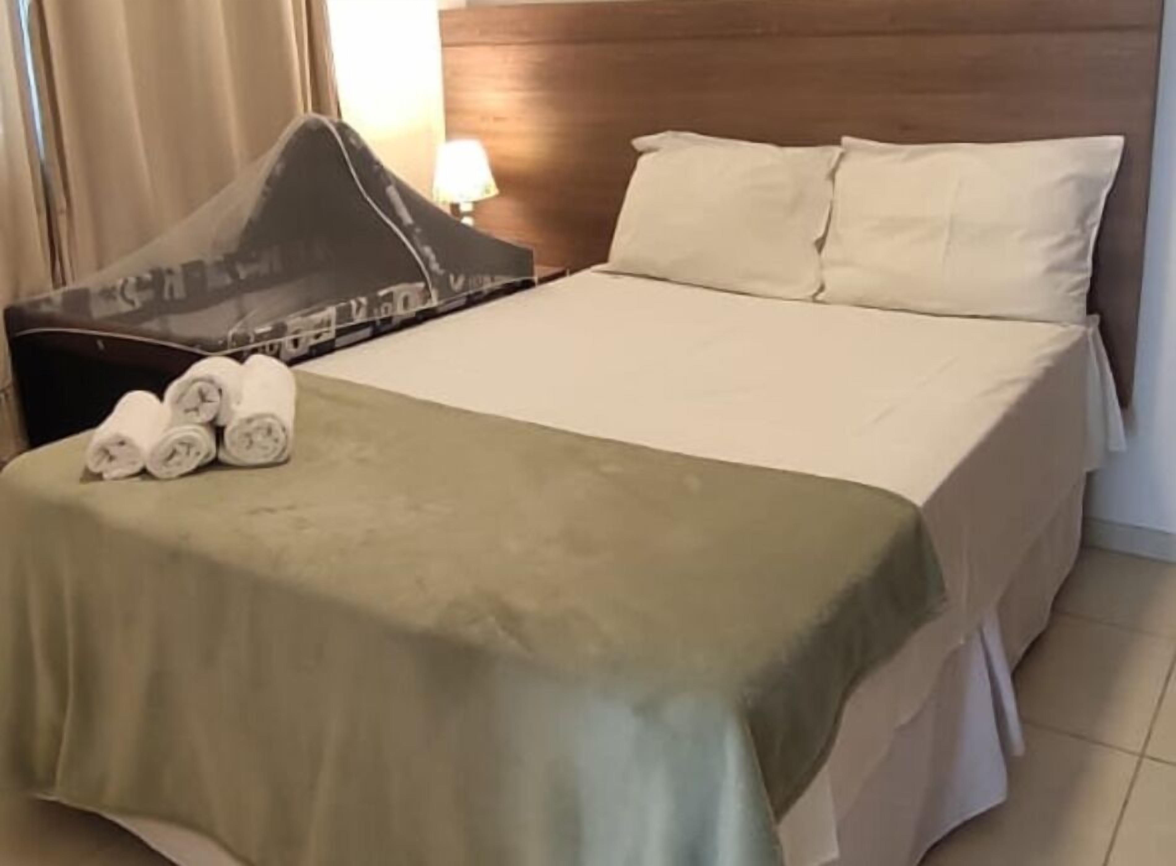 Una cama bien hecha con una colcha verde, dos almohadas y toallas enrolladas a un lado.