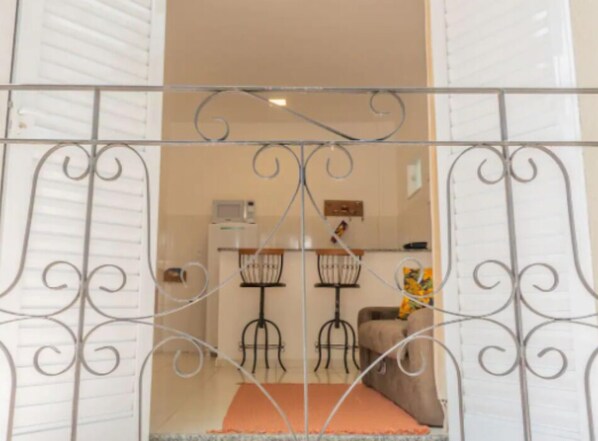 A doorway with decorative metalwork, leading to a room with a kitchenette, two chairs, and a sofa. - Apart Sol Nascente (Itatiaia)