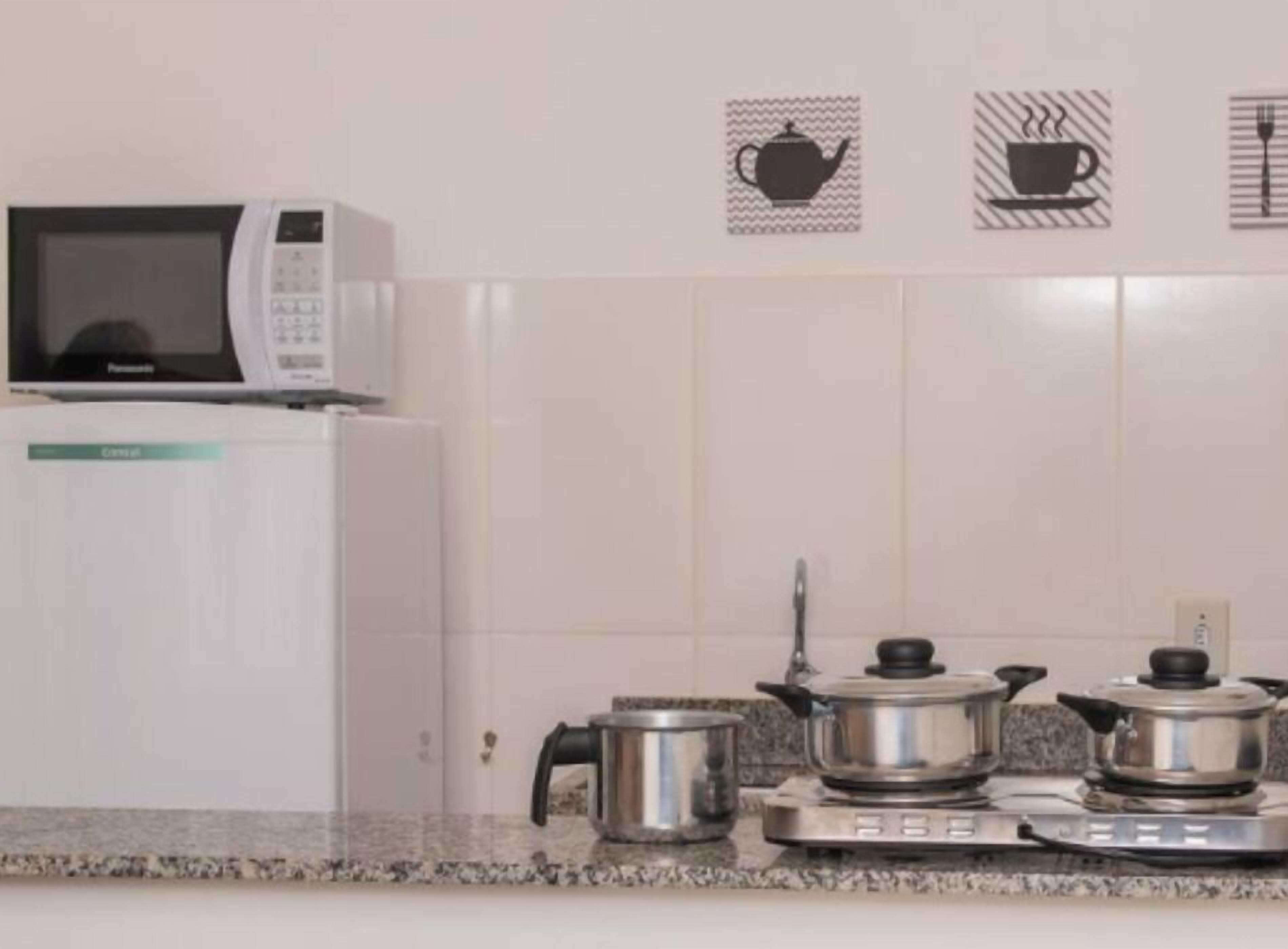 Ett kök med mikrovågsugn, kylsk åp och en spis med kastruller. På väggen finns bilder av en tekanna, en kopp kaffe och en gaffel.