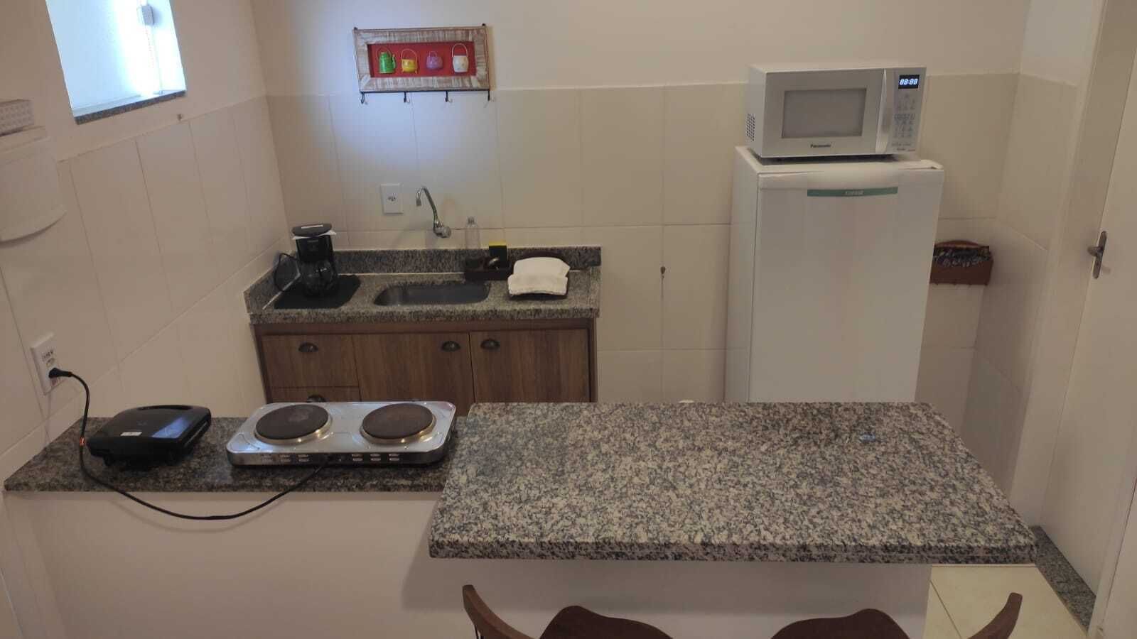 A compact kitchen with a granite countertop, a microwave, a small refrigerator, and a gas stove.