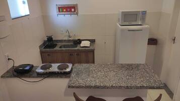 A compact kitchen with a granite countertop, a microwave, a small refrigerator, and a gas stove.