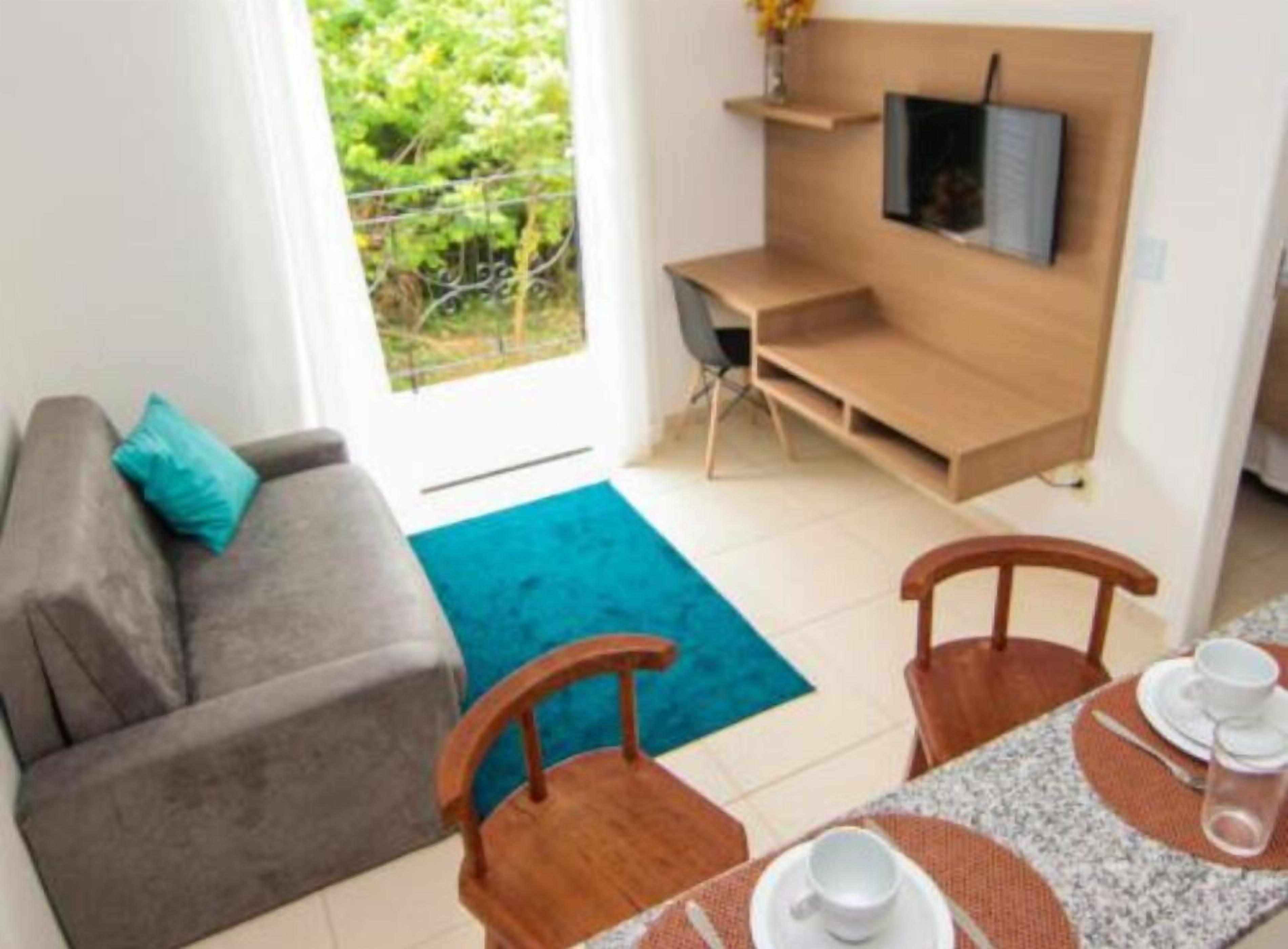 Una sala moderna con un sofá gris, una mesa de comedor de madera dispuesta con platos, tazas y un jarrón de flores. Un televisor está montado en la pared sobre un escritorio de madera.