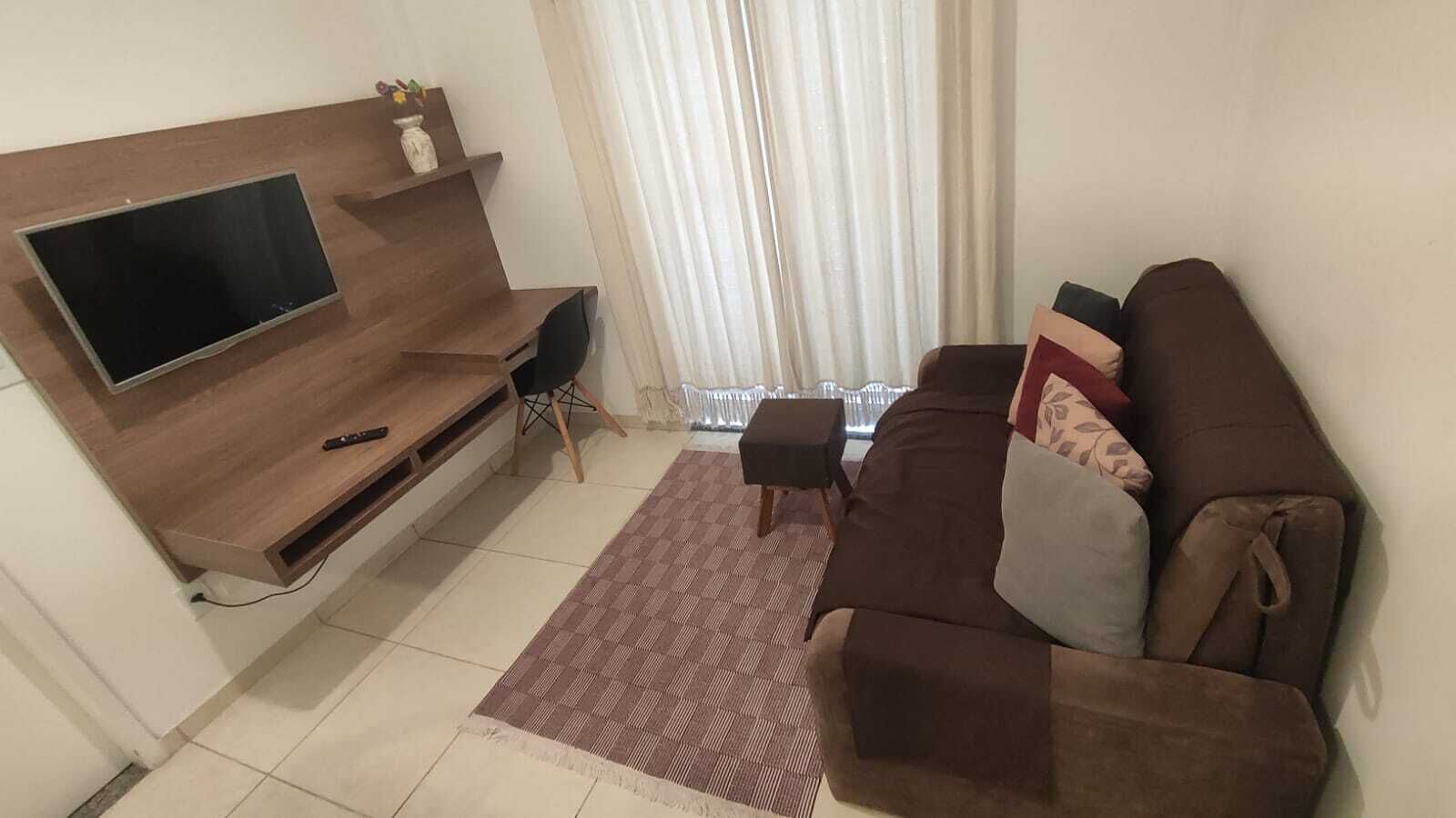 A living room with a flat-screen TV, a brown sofa, a small coffee table, and a patterned rug.