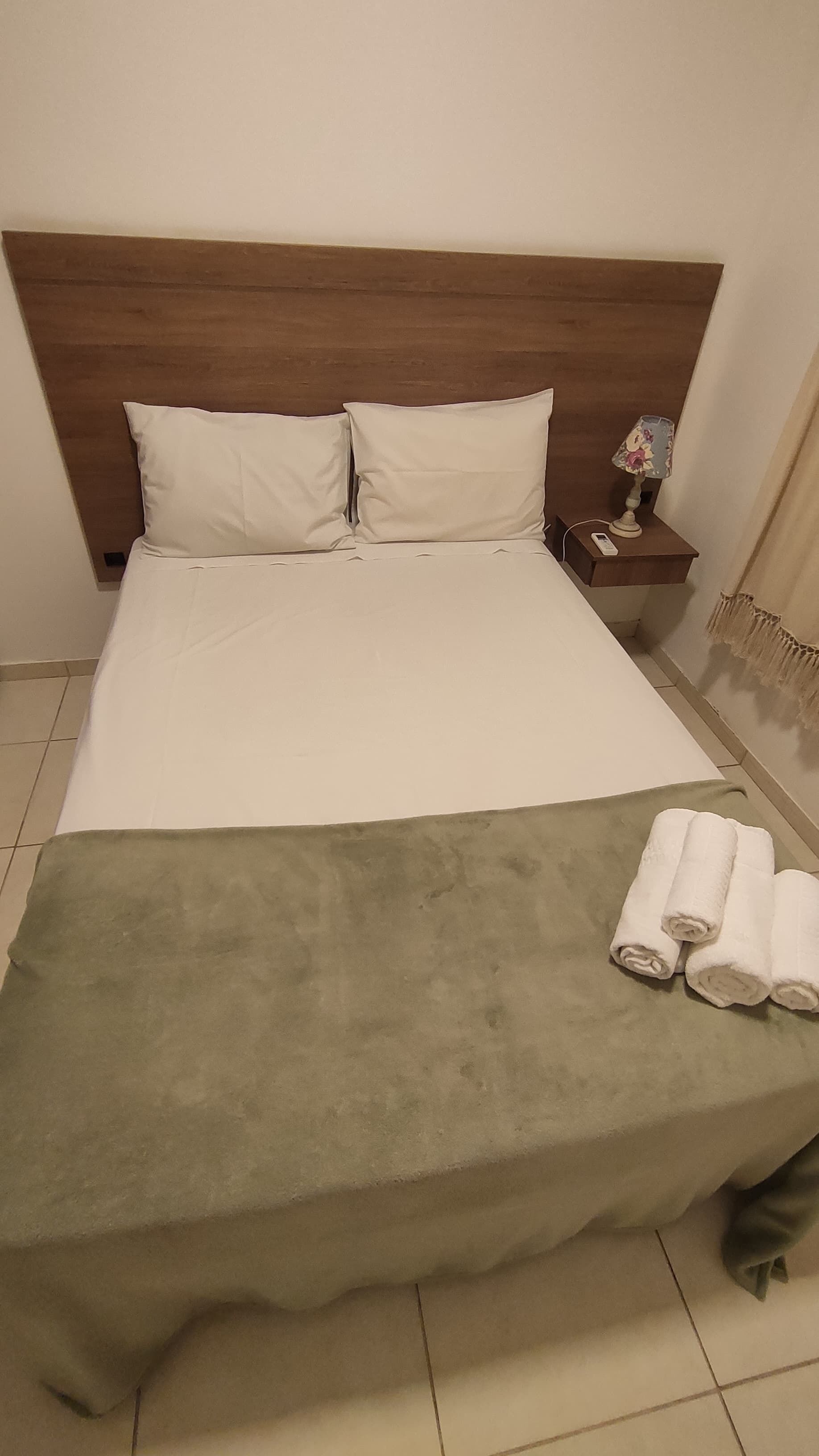 Una cama bien hecha con sábanas blancas, una manta verde y toallas enrolladas a un lado.