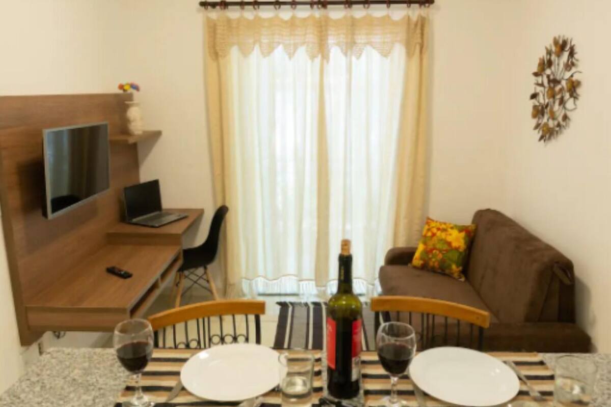 A compact living space with a dining table set for two, a sofa, a TV mounted on the wall, and a curtain covering the window.