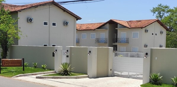 A two-story building with a gated entrance, air conditioning units, and a sign indicating 'Apart Sol Nascimento'. - Apart Sol Nascente (Itatiaia)