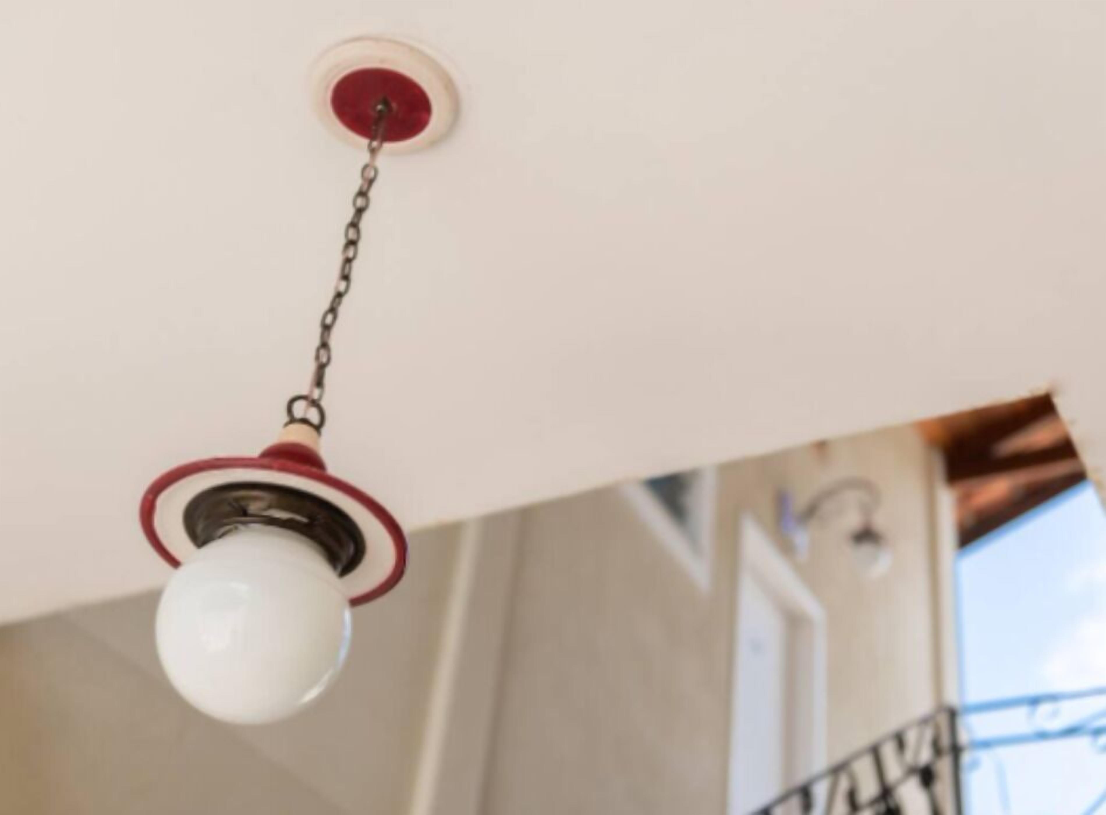A ceiling-mounted light fixture with a white globe and a red ring.