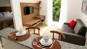 Una sala moderna con comedor, un sofá, un televisor montado en la pared y vistas a zonas verdes al exterior.
