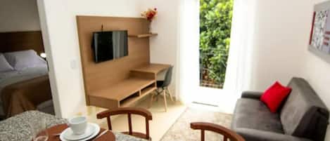 Un salon moderne comprenant un coin repas, un canapé, un téléviseur fixé au mur et une vue sur la verdure à l’extérieur.