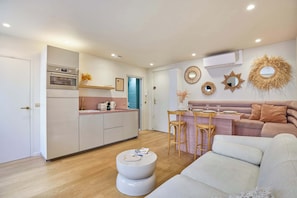 Cozinha moderna com eletrodomésticos embutidos, área de jantar com banco e sala de estar com sofá e apoio para os pés.