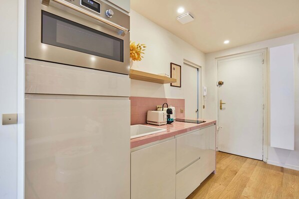 A modern kitchen with stainless steel appliances, a countertop sink, and a wooden shelf.
