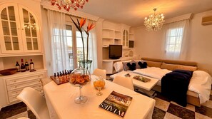 Une pièce bien éclairée et élégamment meublée, avec une table à manger dressée pour le repas, un canapé, un téléviseur et un lustre.