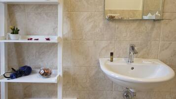 A bathroom with a white sink, a mirror, and shelves with towels and toiletries.