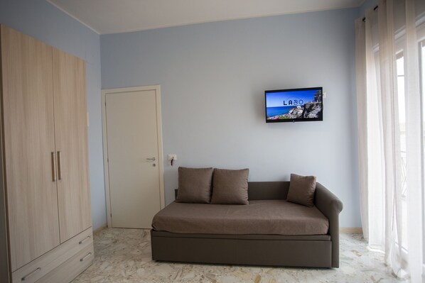 A bedroom with a sofa bed, a wardrobe, a television on the wall, and a door. - Magna Graecia (Tropea)