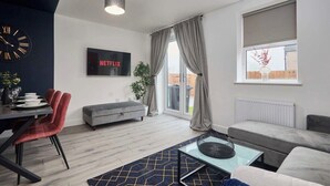 Ein modernes Wohnzimmer mit Essbereich, grauen Sofas, einem Flachbildfernseher und einem großen Fenster mit Vorhängen.