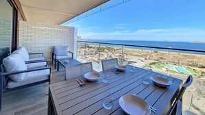Un balcone con tavolo apparecchiato per mangiare, un divano e vista sul mare e sulla città.
