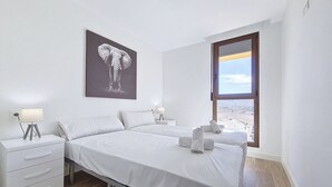 Una camera d'albergo con due letti, un comodino con una lampada, un quadro raffigurante un elefante appeso al muro e una finestra vista paesaggio.