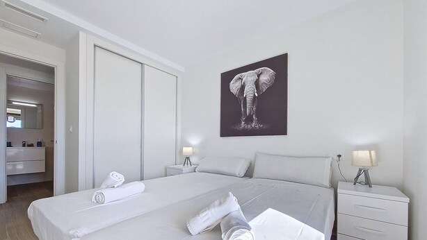 Une chambre d’hôtel avec un grand lit, deux tables de chevet avec des lampes, une armoire et une œuvre d’art représentant un éléphant accrochée au mur.