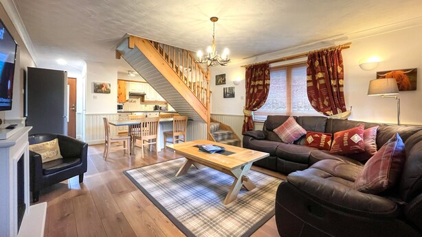 A living room with a sofa, coffee table, and a staircase leading to a kitchen. - Inchmurrin Lodge with private hot tub (Drymen)