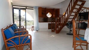 Un vaste espace de vie avec balcon, des meubles en osier, un escalier et un téléviseur.