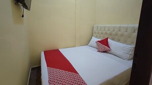 Un petit lit bien fait, avec une couverture rouge et blanche et un seul oreiller rouge.