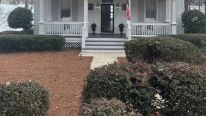 A two-story house with a front porch, a flag, and a well-maintained lawn. - Great Waters gem! Spacious Waterfront Cottage! Family Friendly Getaway! (Eatonton)
