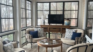 A sunroom with a sofa set, a coffee table, and a television on a wooden stand. - Great Waters gem! Spacious Waterfront Cottage! Family Friendly Getaway! (Eatonton)