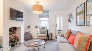 Uma sala de estar com sofá, poltrona, mesa de centro, lareira, televisão e obras de arte nas paredes.