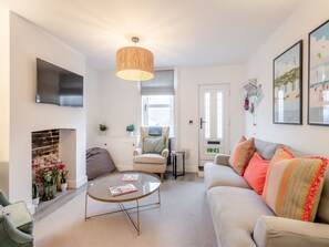 A living room with a sofa, armchair, coffee table, fireplace, television, and artwork on the walls. - 3 bedroom accommodation in Lowestoft (Lowestoft)