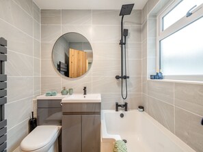 A modern bathroom with a toilet, sink, vanity, bathtub, shower, and a large mirror. - 3 bedroom accommodation in Lowestoft (Lowestoft)