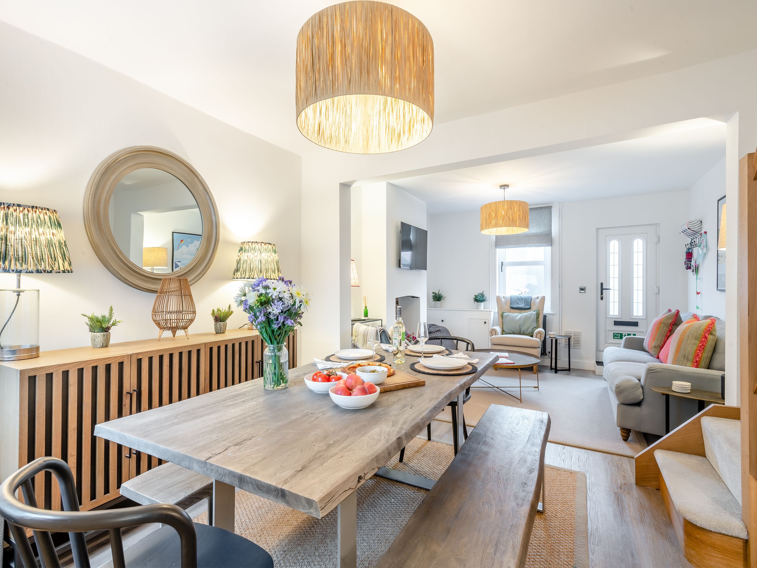 A modern living room with a wooden dining table, a sofa, and a large mirror.