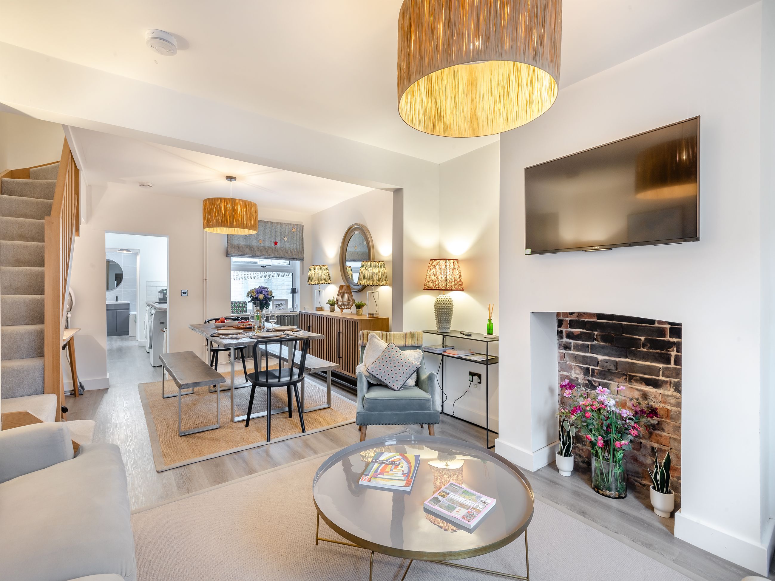 A modern living room with a fireplace, a TV mounted on the wall, and a dining area with a kitchen in the background.